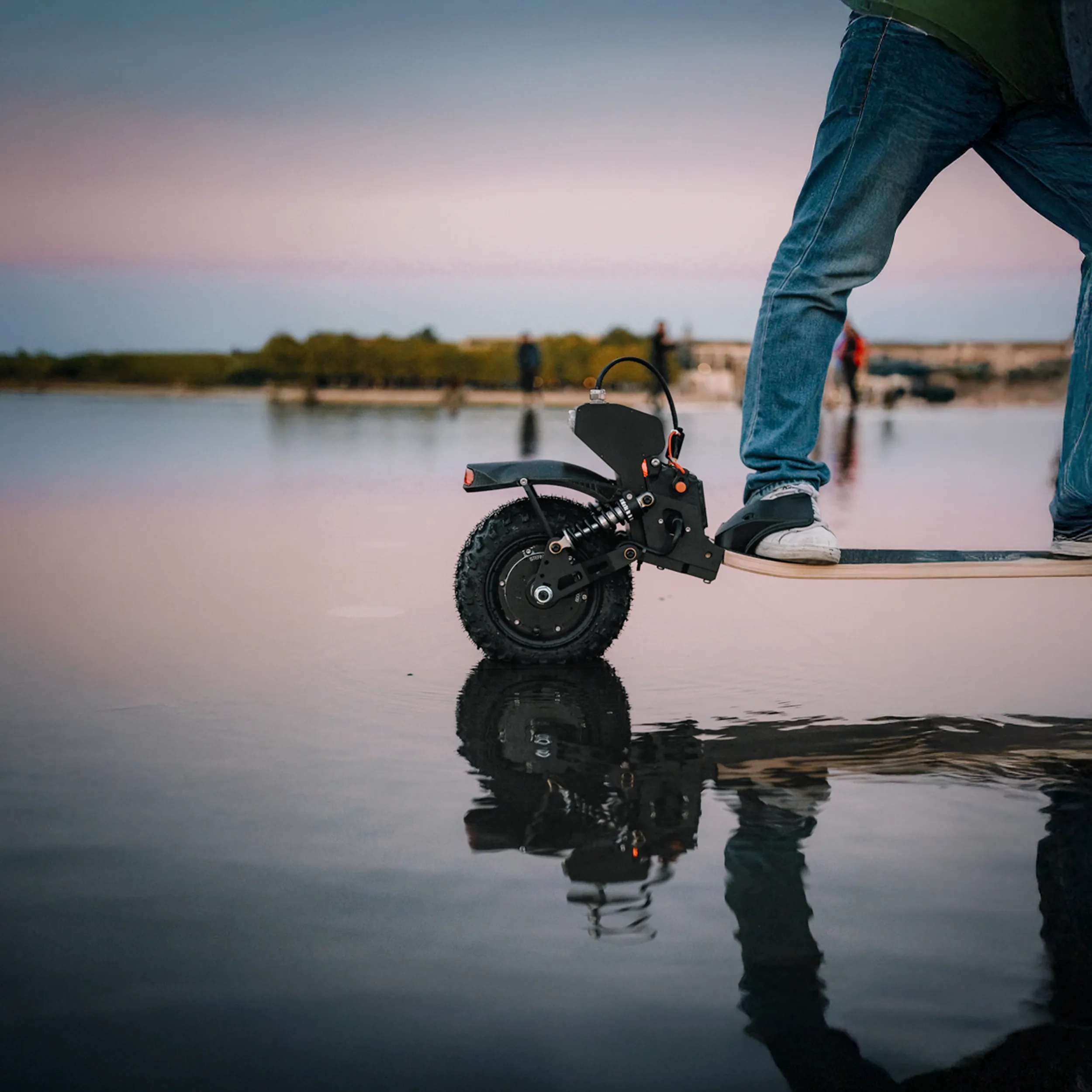 Skateboard eléctrico Sternboard de tres ruedas reflejado en agua tranquila al atardecer