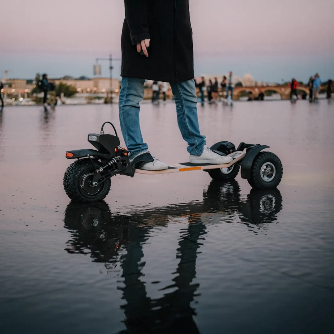 Skateboard eléctrico Sternboard de tres ruedas con batería a la espalda en uso urbano sobre superficie mojada