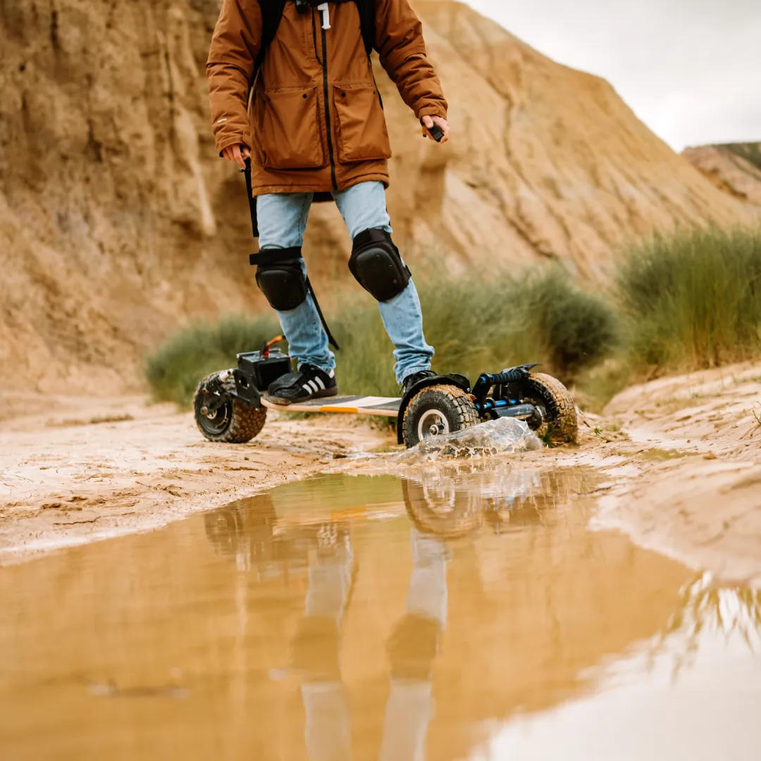 Rider Sternboard equipado con rodilleras atravesando un gran charco de barro con skateboard eléctrico impermeable