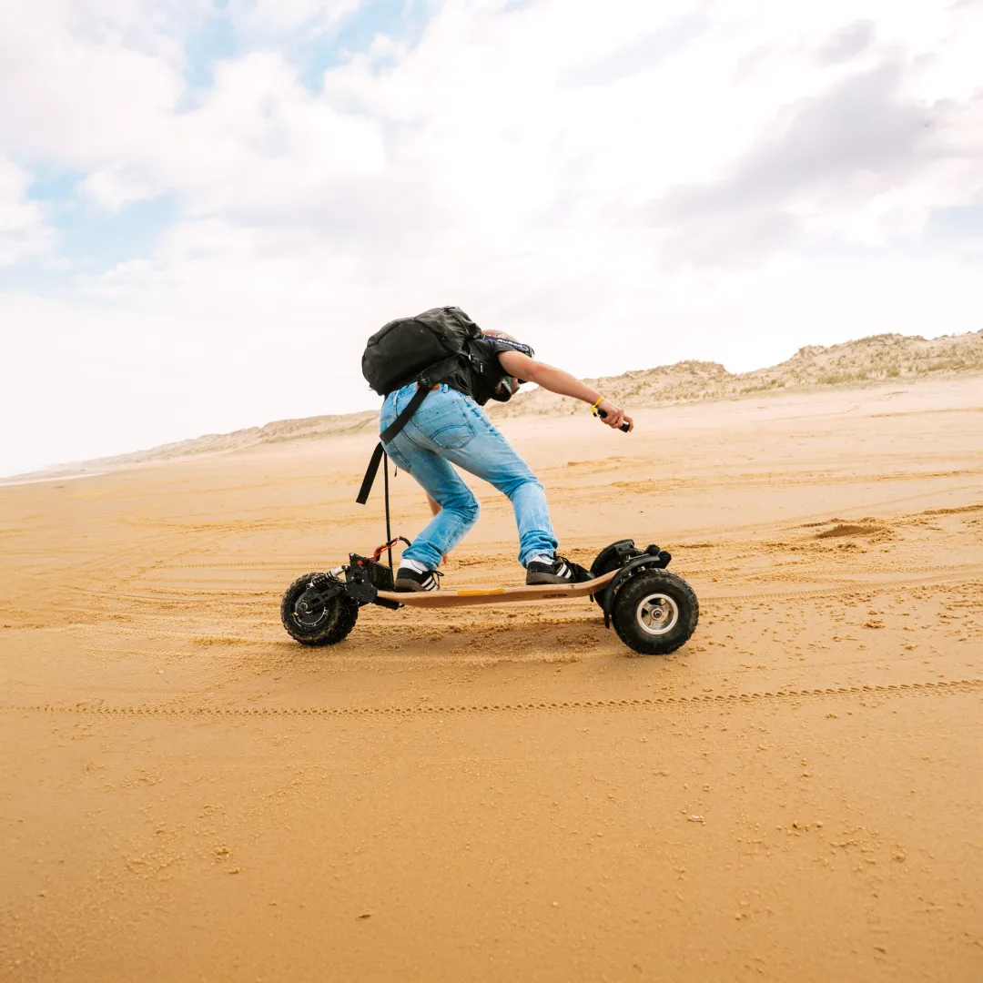 Rider Sternboard realizando un giro dinámico en la playa con skateboard eléctrico de tres ruedas todo terreno