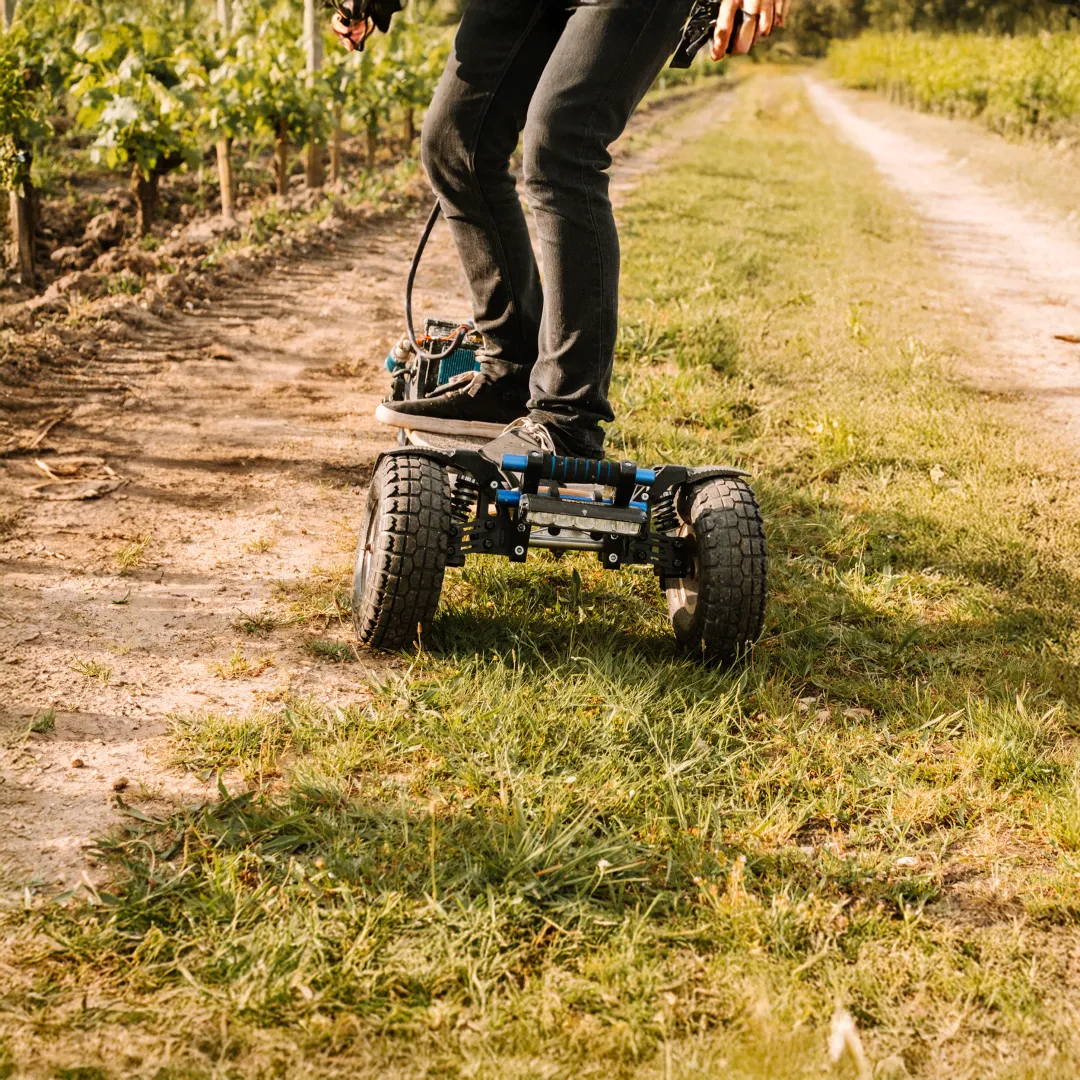 Rider Sternboard recorriendo un camino de viñedo entre tierra y hierba con skateboard eléctrico de tres ruedas
