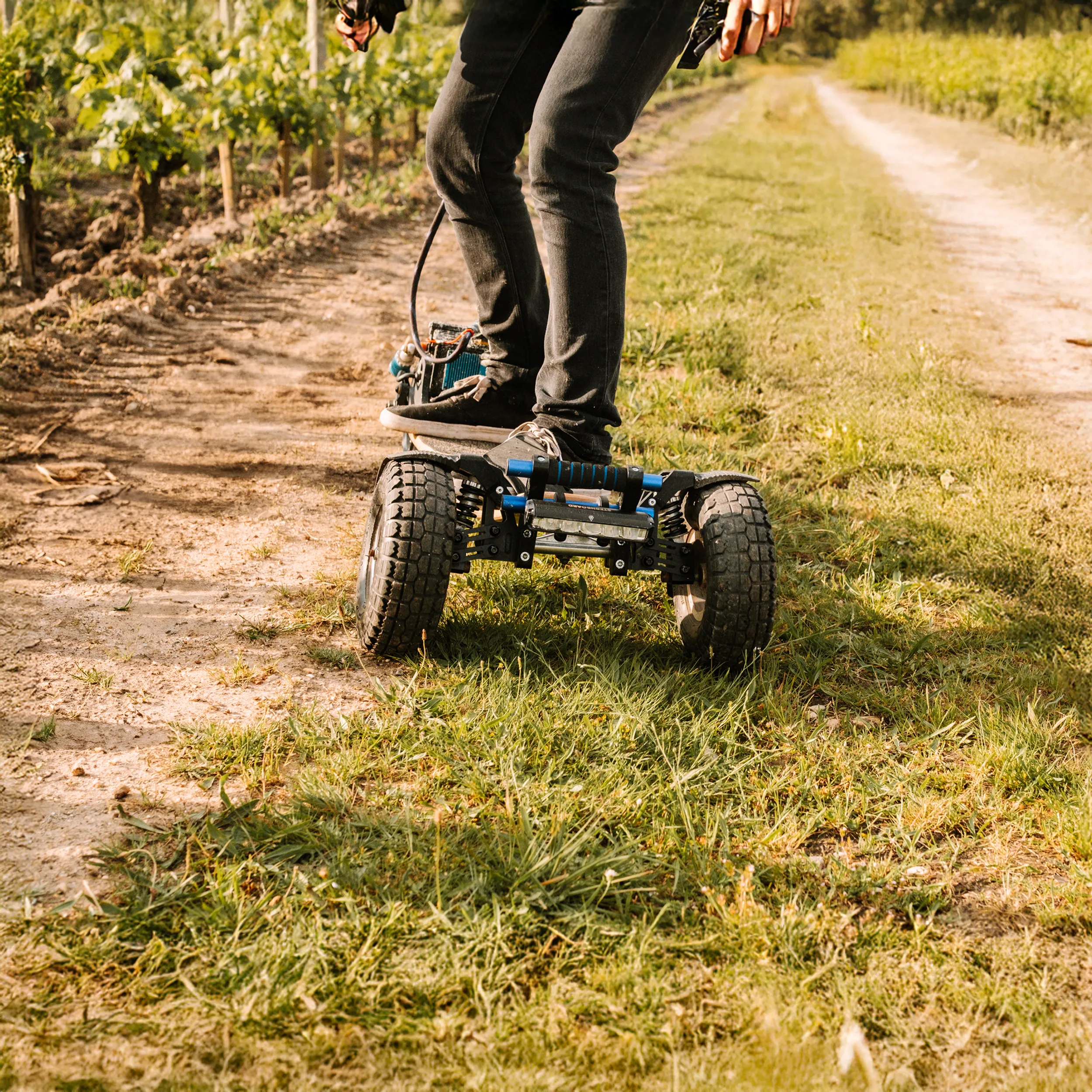 Rider Sternboard recorriendo un camino de viñedo entre tierra y hierba con skateboard eléctrico de tres ruedas