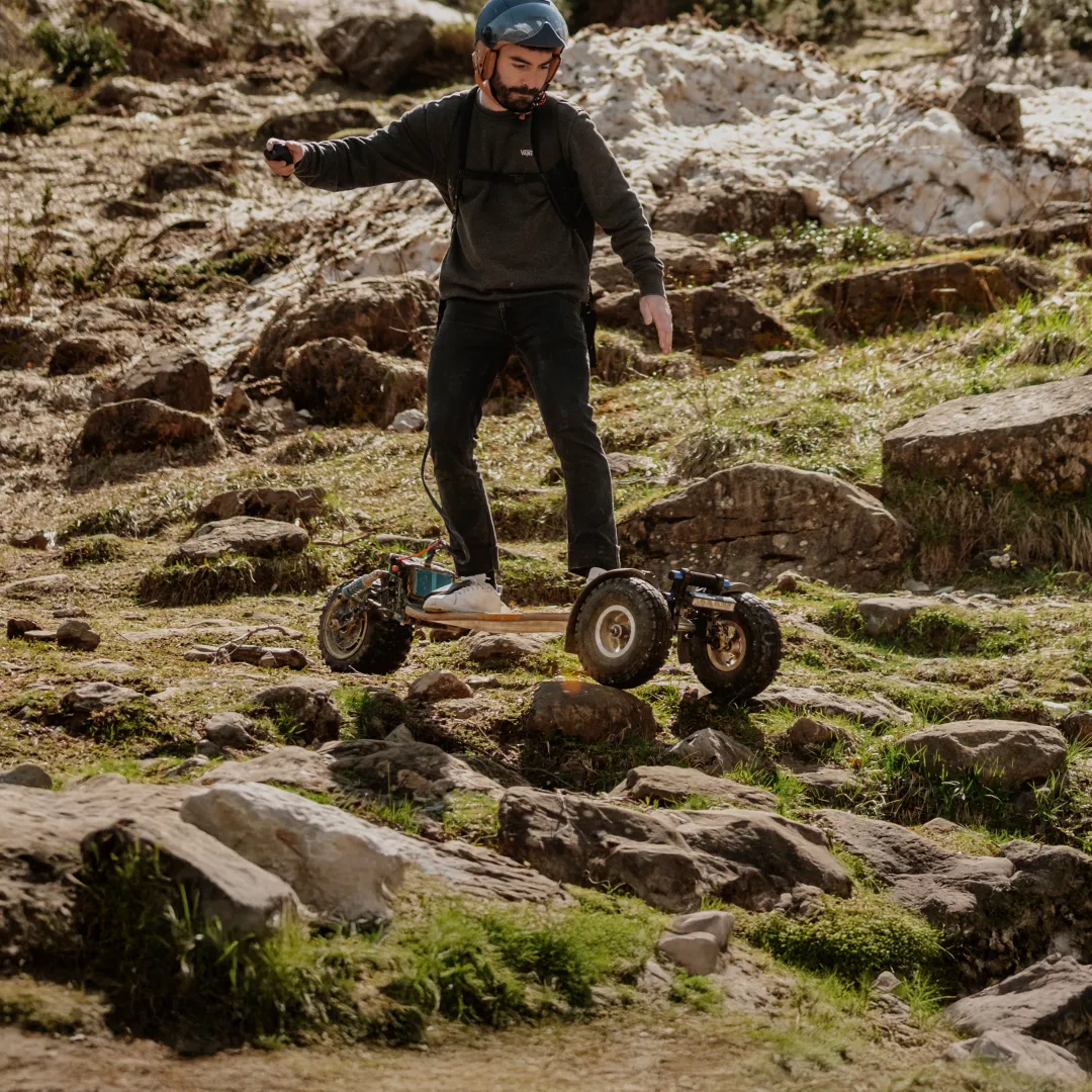 Rider Sternboard equipado con casco atravesando terreno rocoso accidentado con skateboard eléctrico de tres ruedas